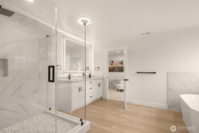 full bath with a marble finish shower, vanity, a freestanding tub, baseboards, and wood finished floors