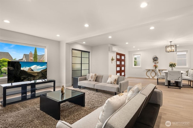 living room featuring light wood-style floors, recessed lighting, an AC wall unit, baseboards, and a chandelier