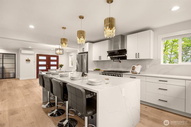 kitchen featuring freestanding refrigerator, a wall mounted AC, wall chimney range hood, recessed lighting, and light wood-type flooring