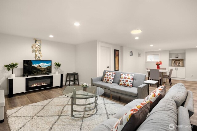 living area with recessed lighting, wood finished floors, a glass covered fireplace, and baseboards