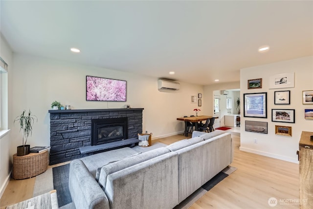 living room with a wall mounted AC, light wood-type flooring, baseboards, a stone fireplace, and recessed lighting