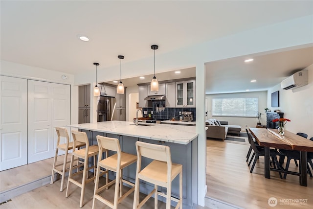 kitchen with stainless steel fridge with ice dispenser, an AC wall unit, light wood-style flooring, gray cabinets, and a kitchen breakfast bar