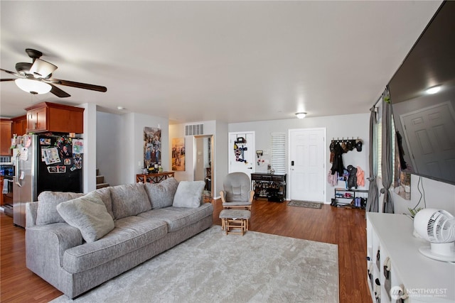 living room featuring wood finished floors, a ceiling fan, and stairs