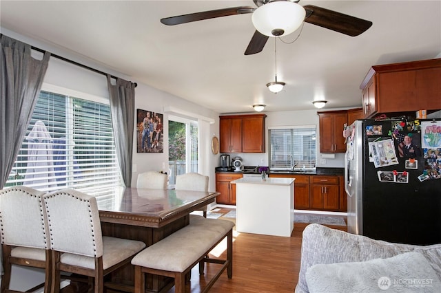 kitchen with stainless steel refrigerator with ice dispenser, dark wood finished floors, a kitchen island, brown cabinets, and ceiling fan