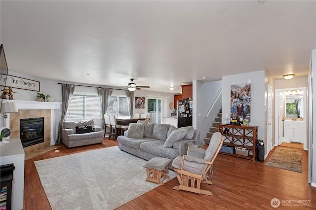 living room with wood finished floors, stairway, a fireplace, and ceiling fan