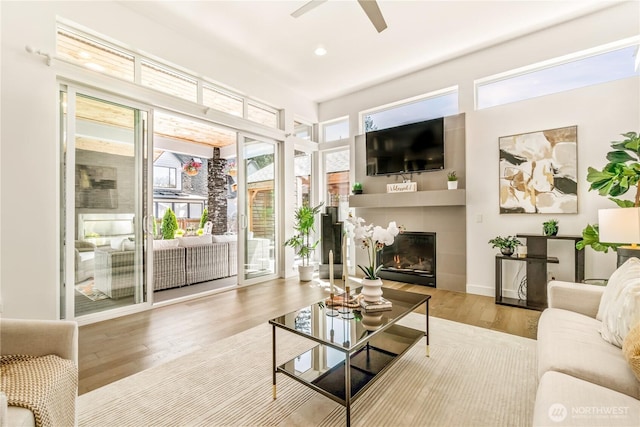 living area featuring wood finished floors, ceiling fan, a glass covered fireplace, and recessed lighting