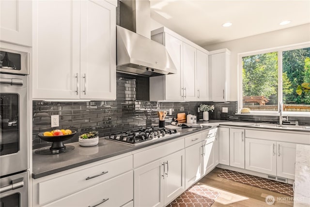 kitchen featuring wall chimney exhaust hood, a sink, white cabinets, stainless steel gas stovetop, and tasteful backsplash