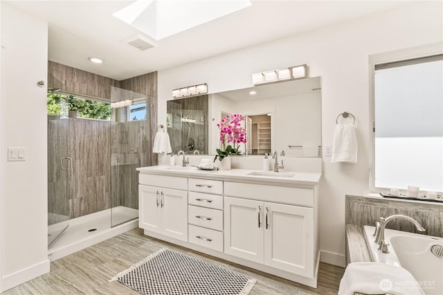 full bathroom with a shower stall, double vanity, a garden tub, and a skylight