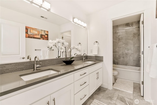 full bathroom with marble look tiles, toilet, double vanity, and shower / bath combination