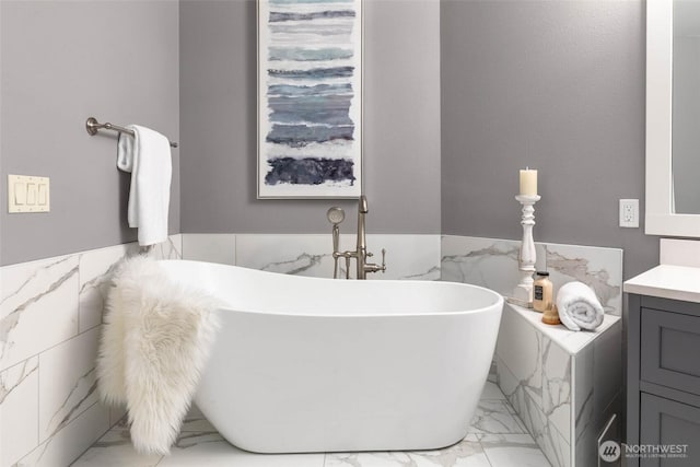 bathroom featuring marble look tiles, tile walls, a wainscoted wall, vanity, and a freestanding tub