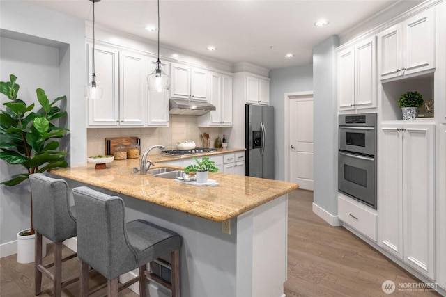kitchen with appliances with stainless steel finishes, under cabinet range hood, a peninsula, white cabinets, and a breakfast bar area