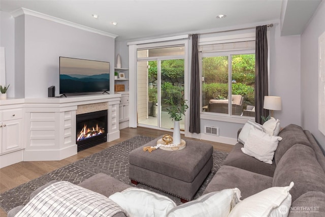 living room featuring wood finished floors, a lit fireplace, crown molding, and recessed lighting