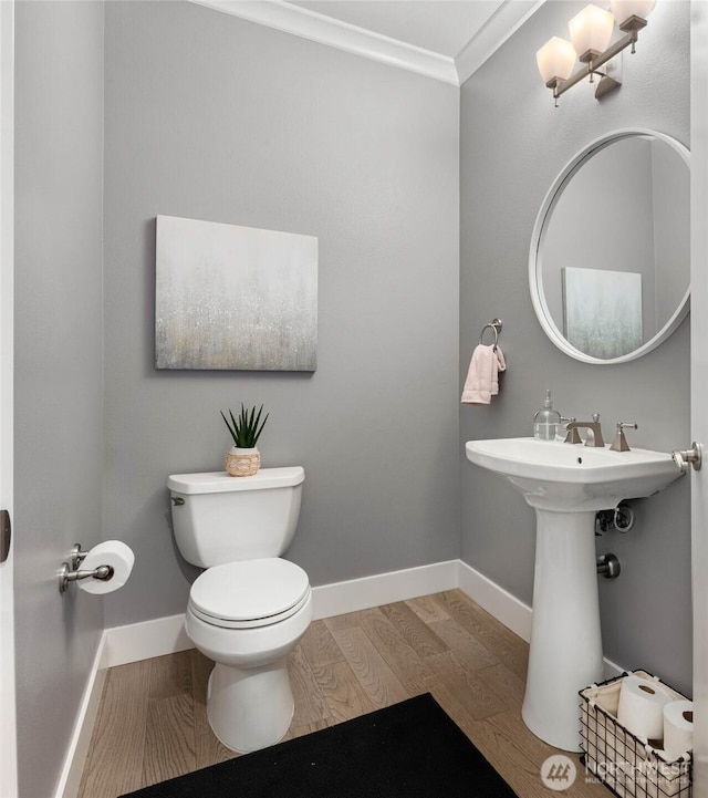 half bathroom with wood finished floors, toilet, crown molding, and baseboards