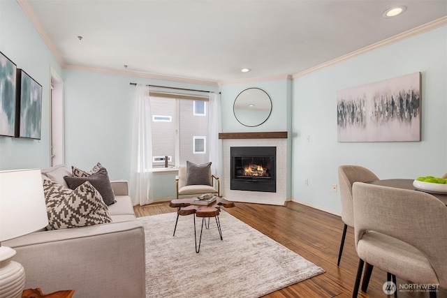 living room featuring crown molding, a glass covered fireplace, wood finished floors, baseboards, and recessed lighting