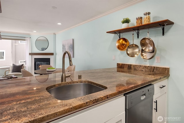 kitchen with stainless steel dishwasher, a sink, white cabinets, dark stone counters, and ornamental molding