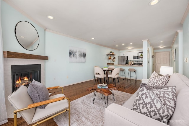 living area featuring ornamental molding, wood finished floors, recessed lighting, a brick fireplace, and baseboards
