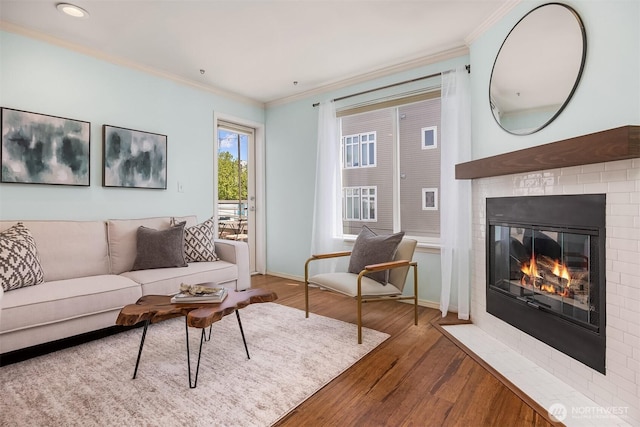 living room featuring crown molding, wood finished floors, a fireplace with flush hearth, and baseboards