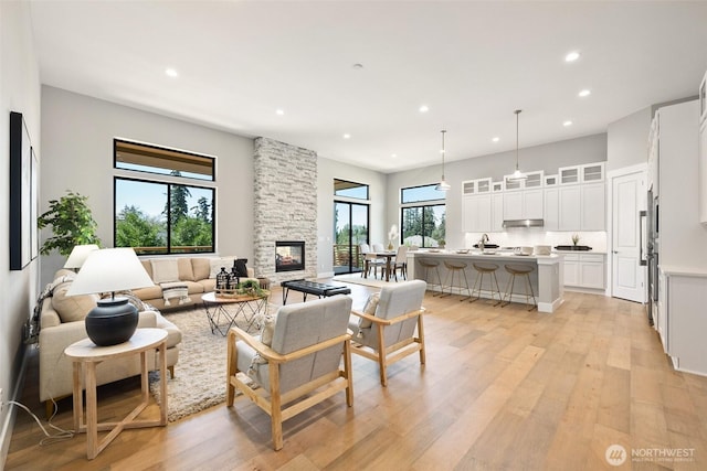 living room featuring recessed lighting, light wood-style flooring, and a stone fireplace