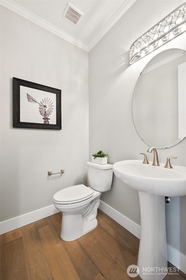 half bathroom with crown molding, baseboards, wood finished floors, toilet, and a sink