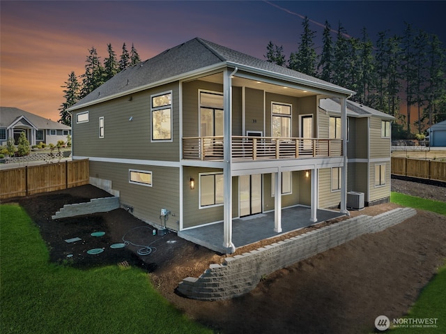 back of property at dusk with a balcony, cooling unit, a patio, and fence