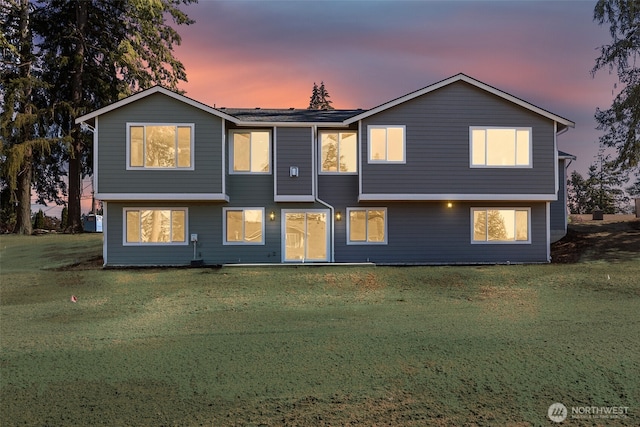 back of house at dusk featuring a lawn