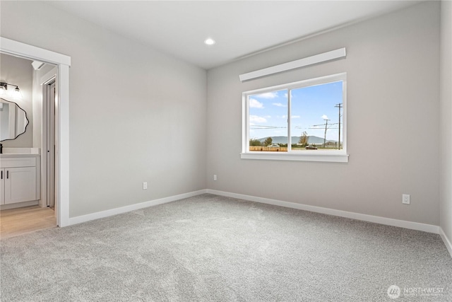 unfurnished bedroom with light colored carpet, baseboards, recessed lighting, and ensuite bath