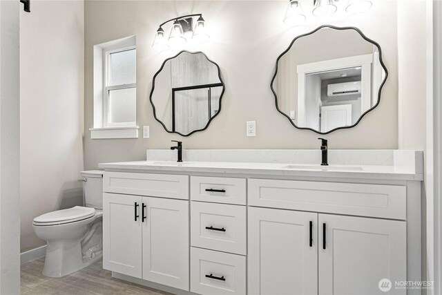 full bathroom featuring an AC wall unit, toilet, wood finished floors, double vanity, and baseboards
