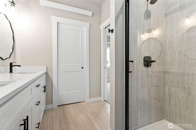 bathroom featuring a tile shower, wood finished floors, baseboards, and double vanity