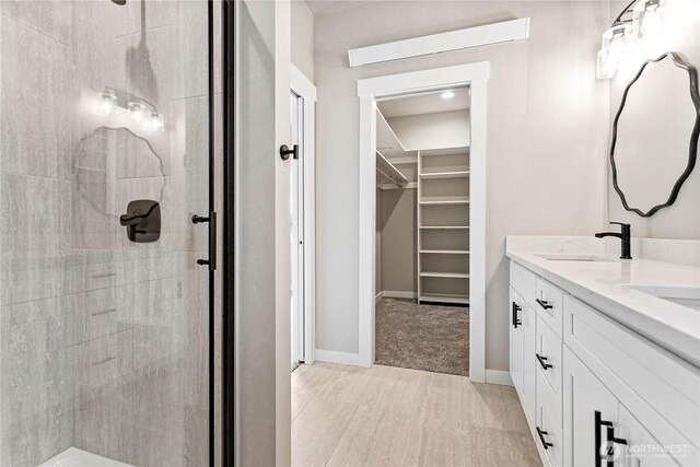 bathroom with a tile shower, a spacious closet, double vanity, and wood finished floors