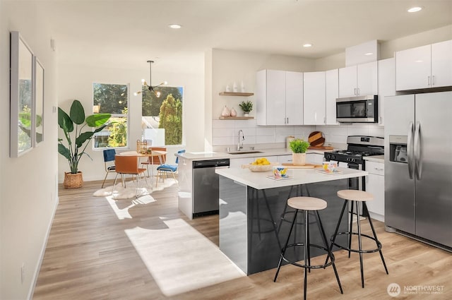 kitchen featuring appliances with stainless steel finishes, open shelves, a sink, a kitchen island, and tasteful backsplash