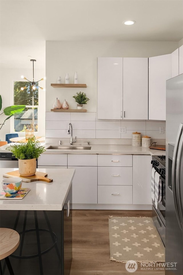 kitchen with a sink, gas range oven, stainless steel fridge, white cabinets, and recessed lighting