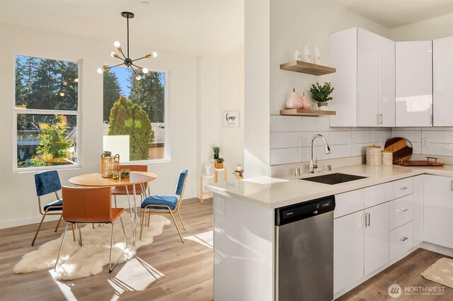 kitchen with stainless steel dishwasher, a sink, open shelves, light countertops, and light wood finished floors