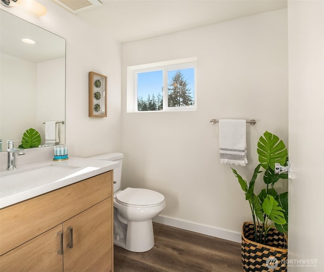 half bath featuring wood finished floors, vanity, toilet, and baseboards