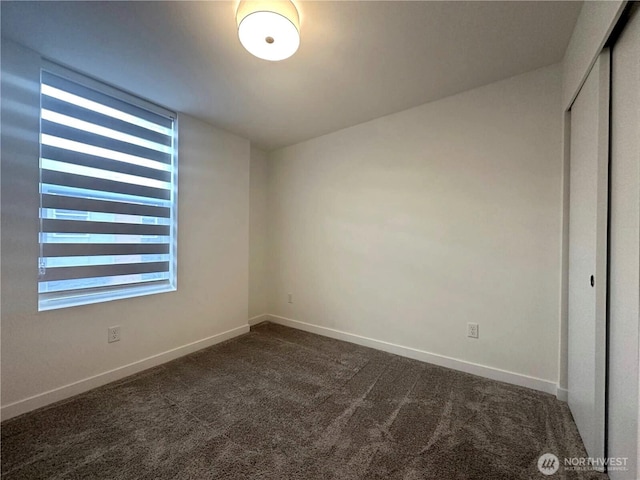 unfurnished room featuring dark carpet and baseboards