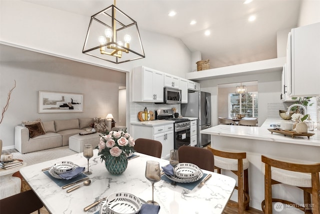 kitchen with appliances with stainless steel finishes, a chandelier, tasteful backsplash, a kitchen breakfast bar, and white cabinetry