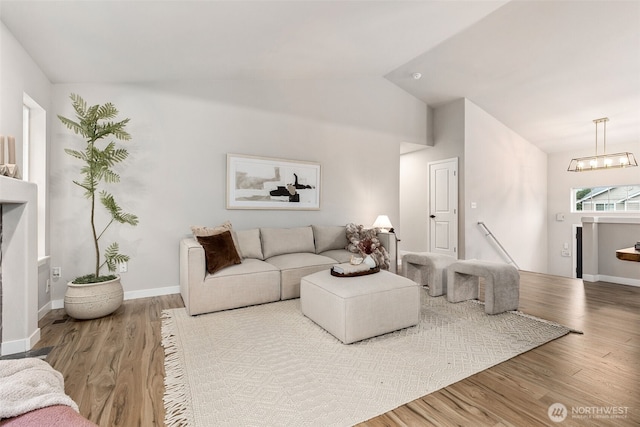 living area with wood finished floors, lofted ceiling, baseboards, and a chandelier