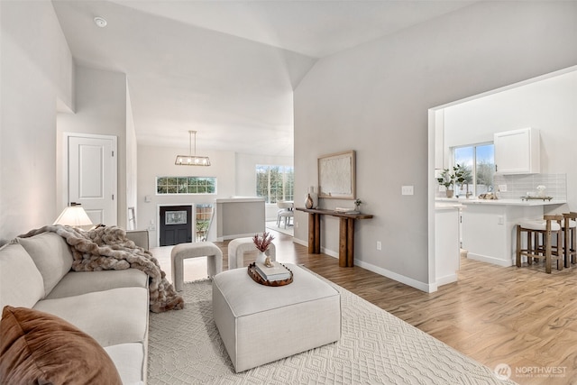 living room featuring light wood finished floors, a chandelier, lofted ceiling, and baseboards