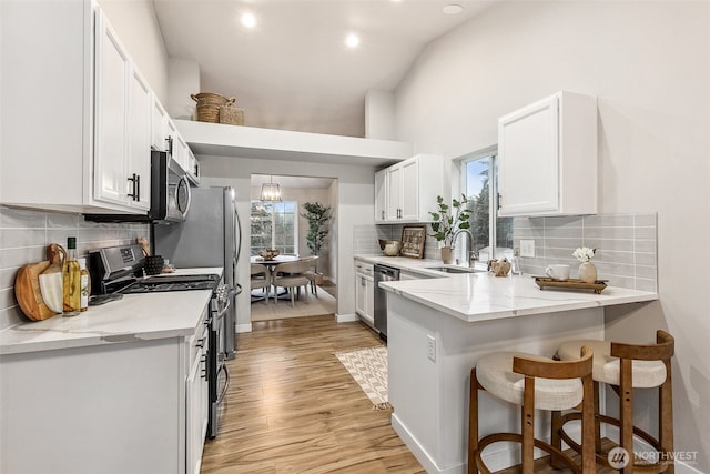kitchen with stainless steel appliances, a sink, white cabinets, a breakfast bar area, and light wood-style flooring