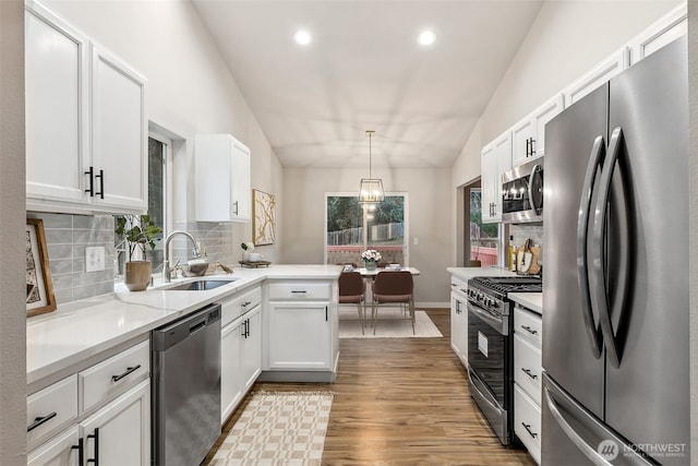 kitchen with appliances with stainless steel finishes, a sink, tasteful backsplash, white cabinetry, and a peninsula