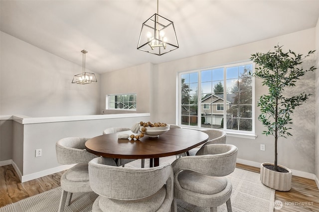 dining room with a chandelier, plenty of natural light, wood finished floors, vaulted ceiling, and baseboards