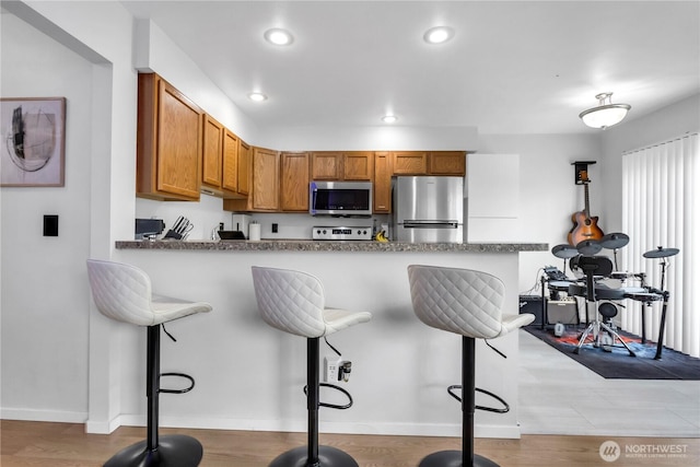 kitchen with appliances with stainless steel finishes, a kitchen bar, brown cabinetry, recessed lighting, and a peninsula