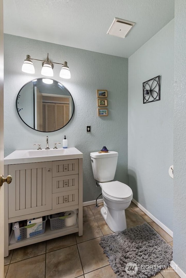 bathroom with vanity, toilet, tile patterned floors, a textured wall, and baseboards