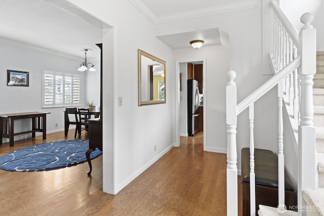 foyer entrance featuring wood finished floors, crown molding, a chandelier, baseboards, and stairs