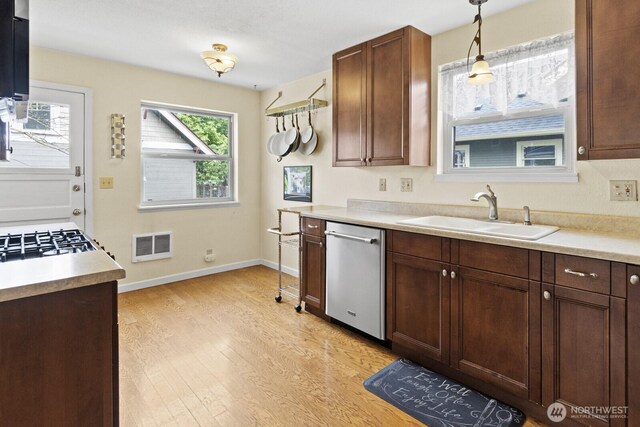 kitchen with a sink, dishwasher, light wood-type flooring, and light countertops