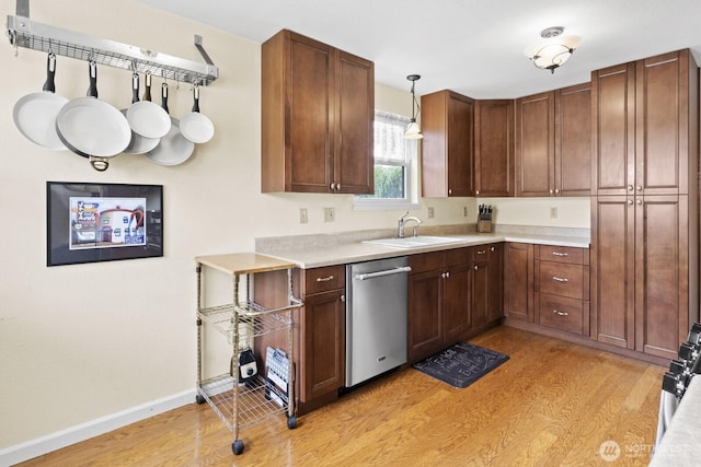 kitchen with stainless steel dishwasher, a sink, light wood-style floors, and light countertops