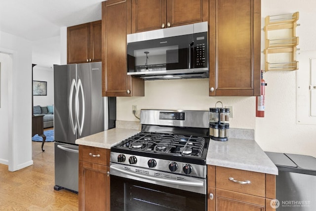 kitchen featuring appliances with stainless steel finishes, light countertops, light wood-style flooring, and brown cabinetry