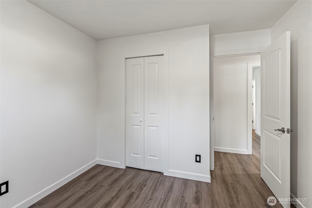 unfurnished bedroom featuring wood finished floors, baseboards, and a closet