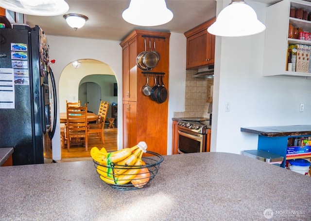 1803 Juniper St, Oroville, WA 98844 - kitchen featuring black fridge, arched walkways, under cabinet range hood, stainless steel electric stove, and brown cabinets