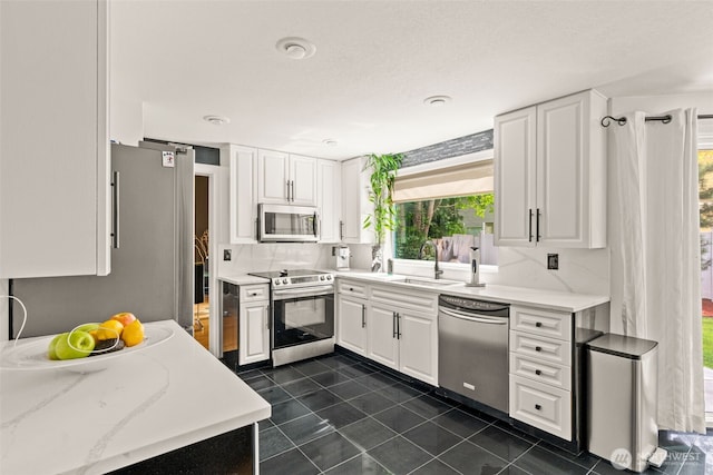 kitchen with stainless steel appliances, a sink, dark tile patterned flooring, white cabinets, and backsplash