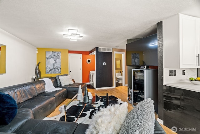 living room featuring washer / dryer, light wood-type flooring, and a textured ceiling
